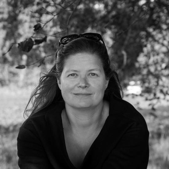 Portrætbillede af Sara Koch i sort/hvid. Hun sidder foran et træ med solbriller i håret.