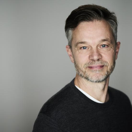 Jesper ser direkte ind i kameraet med et let smil på læberne. Han er iført en sort sweatshirt.