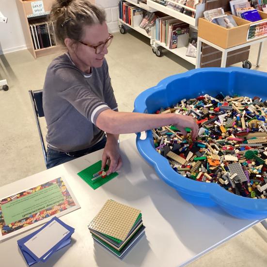Bibliotekaren sidder ved et bord og bygger med LEGO