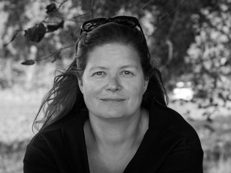 Portrætbillede af Sara Koch i sort/hvid. Hun sidder foran et træ med solbriller i håret.