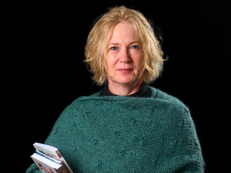 Camilla står med en par bøger i favnen og med en grønligt strikket sjal om skuldrene