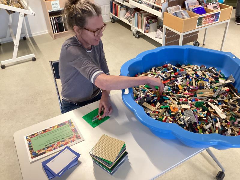 Bibliotekaren sidder ved et bord og bygger med LEGO