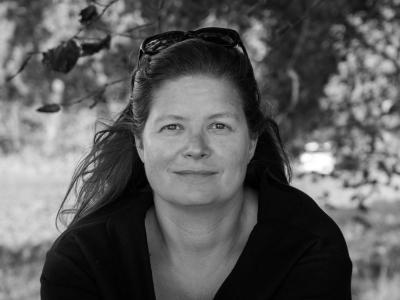 Portrætbillede af Sara Koch i sort/hvid. Hun sidder foran et træ med solbriller i håret.