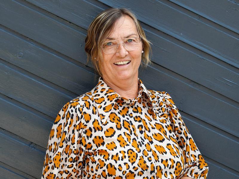 Susanne holder en stak bøger og står foran en sort facade