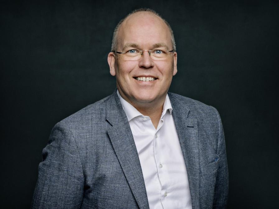 Portrætfoto af Poul Duedahl iført hvid skjorte og gråt jakkesæt.