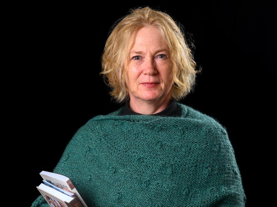 Camilla står med en par bøger i favnen og med en grønligt strikket sjal om skuldrene