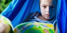 et barn i en blå hængekøje, som læser en spændende bog